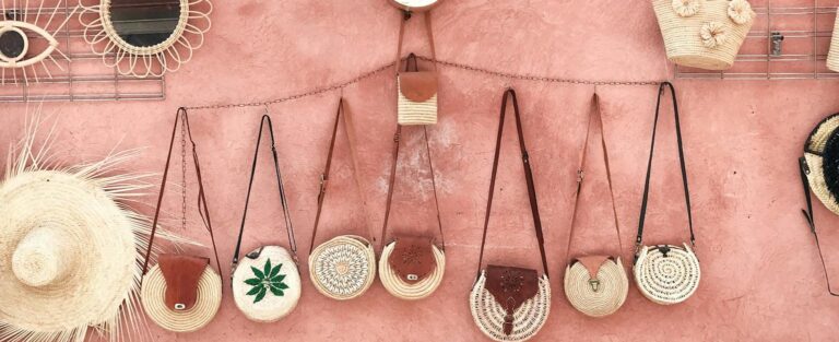 Aesthetic display of handmade wicker and straw accessories against a textured pink wall.