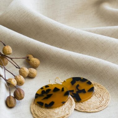 Close-up of unique tortoiseshell and woven earrings on textured fabric, perfect for fashion accessories.