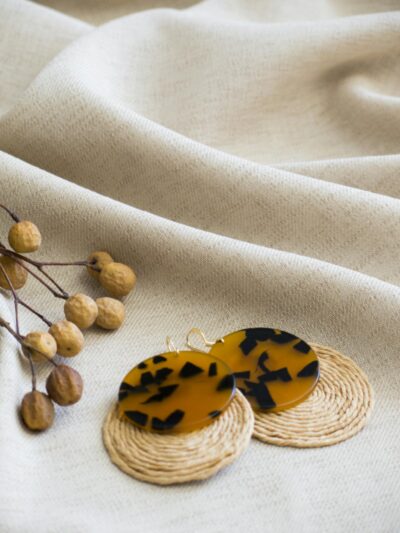 Close-up of unique tortoiseshell and woven earrings on textured fabric, perfect for fashion accessories.